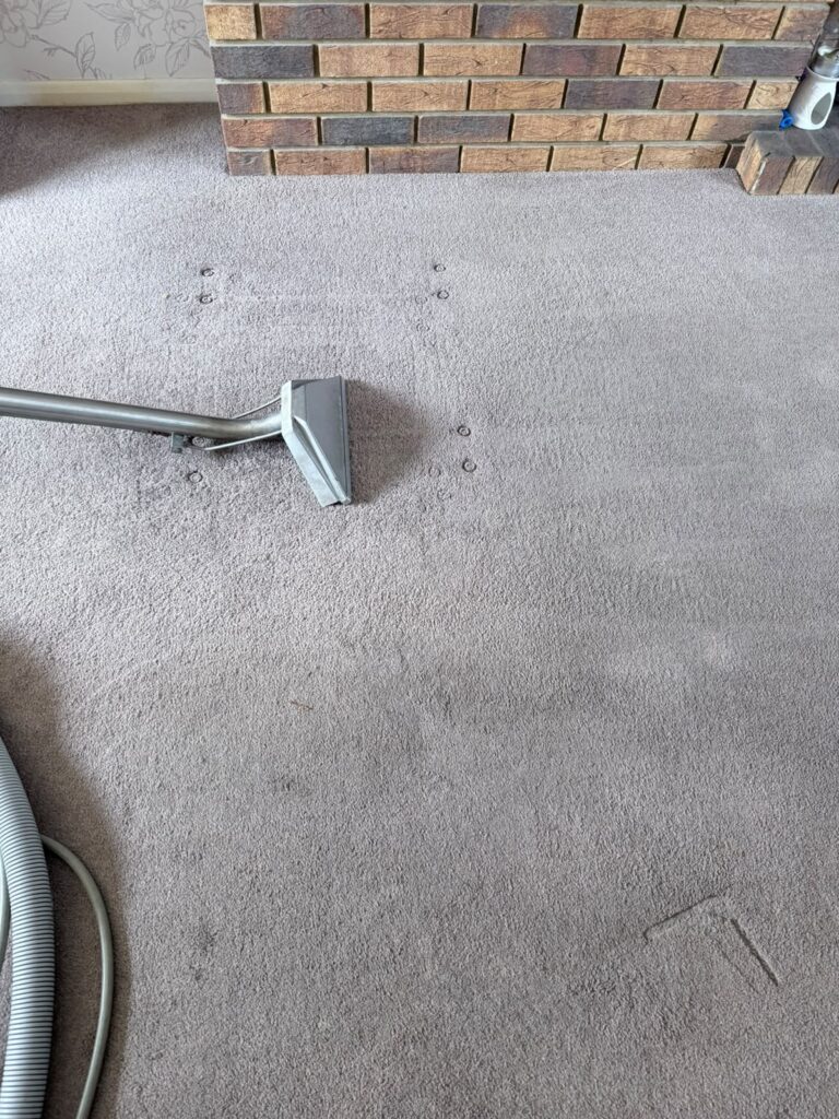 Living room carpet being deep-cleaned with an extraction wand beside a brick fireplace